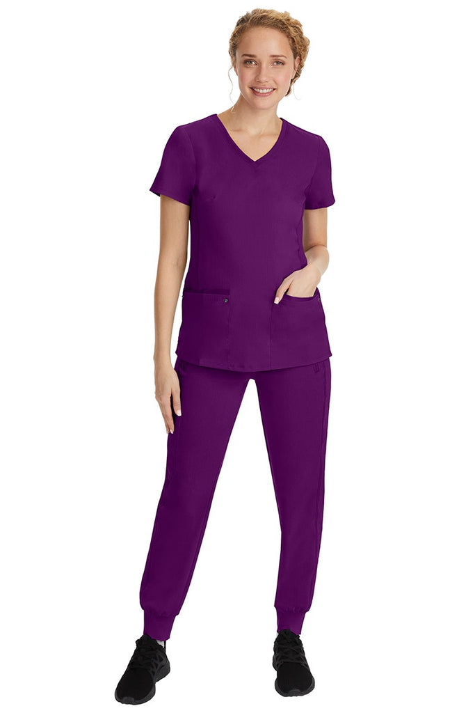 A young female nurse wearing a Purple Label Women's Juliet Yoga Scrub Top by Healing Hands in Eggplant featuring a v-neckline.