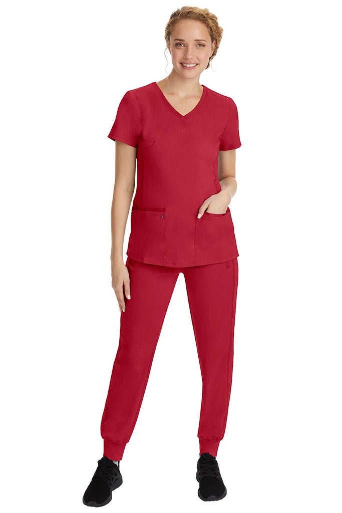 A young female nurse wearing a Purple Label Women's Juliet Yoga Scrub Top by Healing Hands in Red featuring a v-neckline.