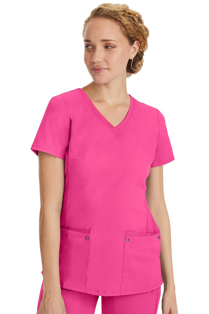 A female healthcare professional wearing a Women's Juliet Yoga Scrub Top from Purple Label in Shocking Pink featuring a side stretch panels.