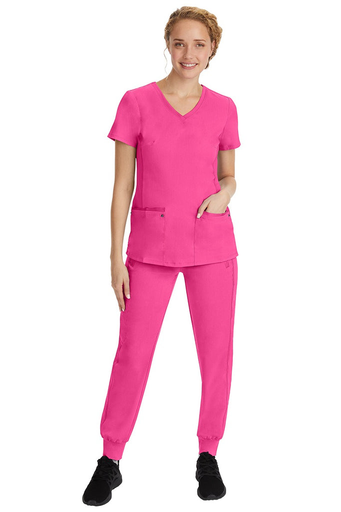 A young female nurse wearing a Purple Label Women's Juliet Yoga Scrub Top by Healing Hands in Shocking Pink  featuring a v-neckline.