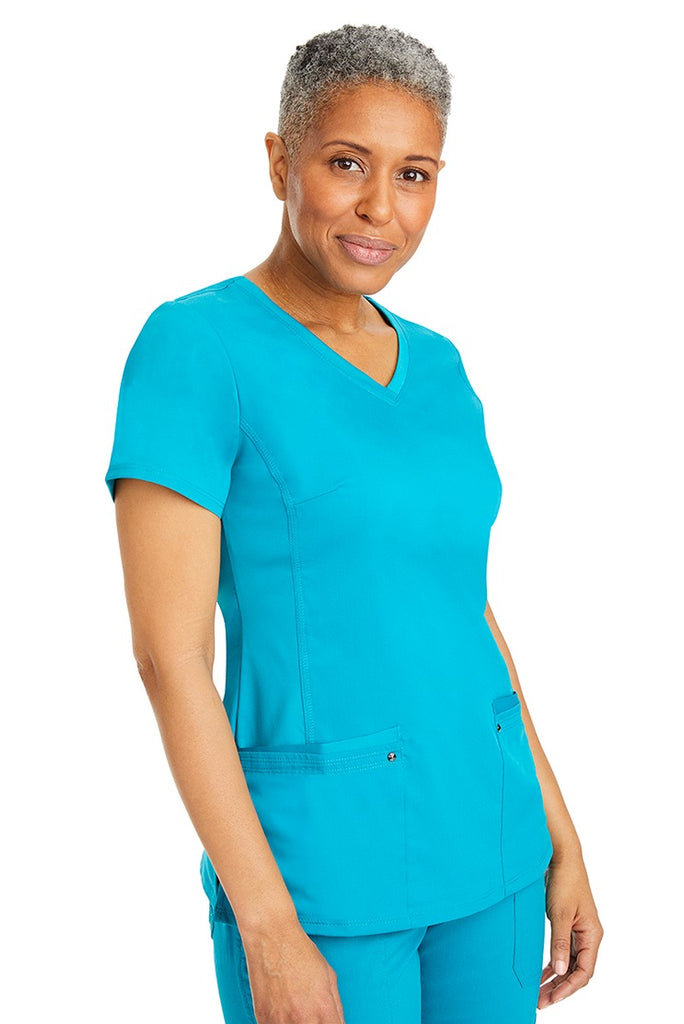 A female healthcare professional wearing a Women's Juliet Yoga Scrub Top from Purple Label in Teal featuring a side stretch panels.