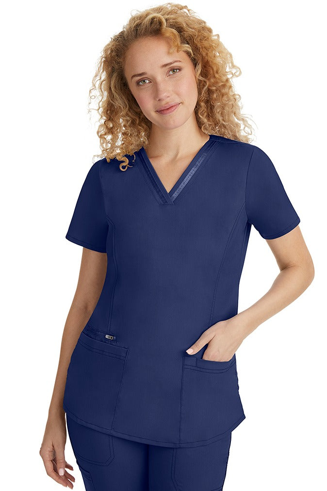A female LPN wearing a Women's Jasmin Fashion V-Neck Scrub Top from Purple Label in Navy featuring side vents at the hem for additional range of motion & to ensure a comfortable all day fit.