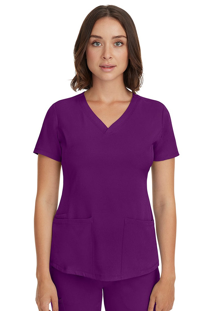 A young female LPN wearing a HH-Works Women's Monica Multi-Pocket Scrub Top in Eggplant featuring short sleeves & a v-neckline.