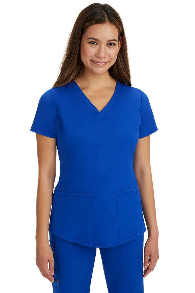A young female LPN wearing a HH-Works Women's Monica Multi-Pocket Scrub Top in Galaxy Blue featuring short sleeves & a v-neckline.