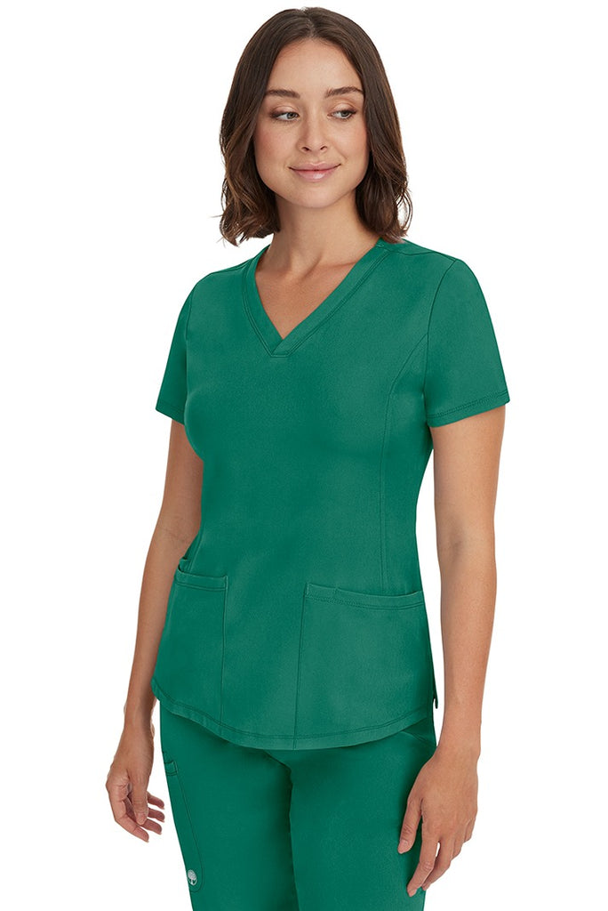 A young female healthcare professional wearing a HH-Works Women's Monica Multi-Pocket Scrub Top in Hunter Green featuring a center back length of 24".