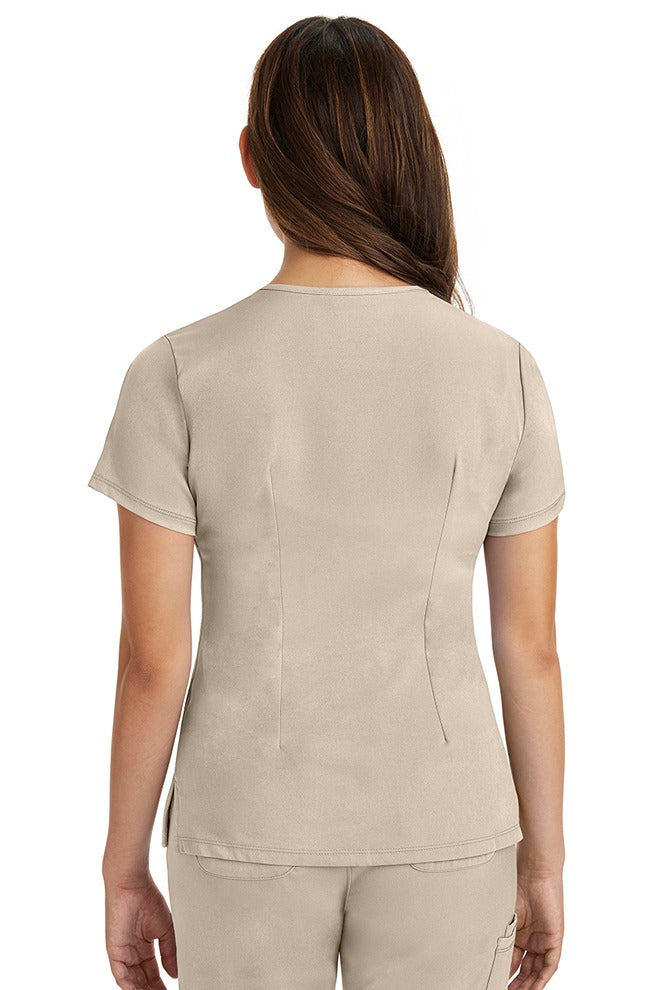 A young female Biller wearing an HH-Works Women's Monica Multi-Pocket Scrub Top in Khaki size Small featuring back bust darts.