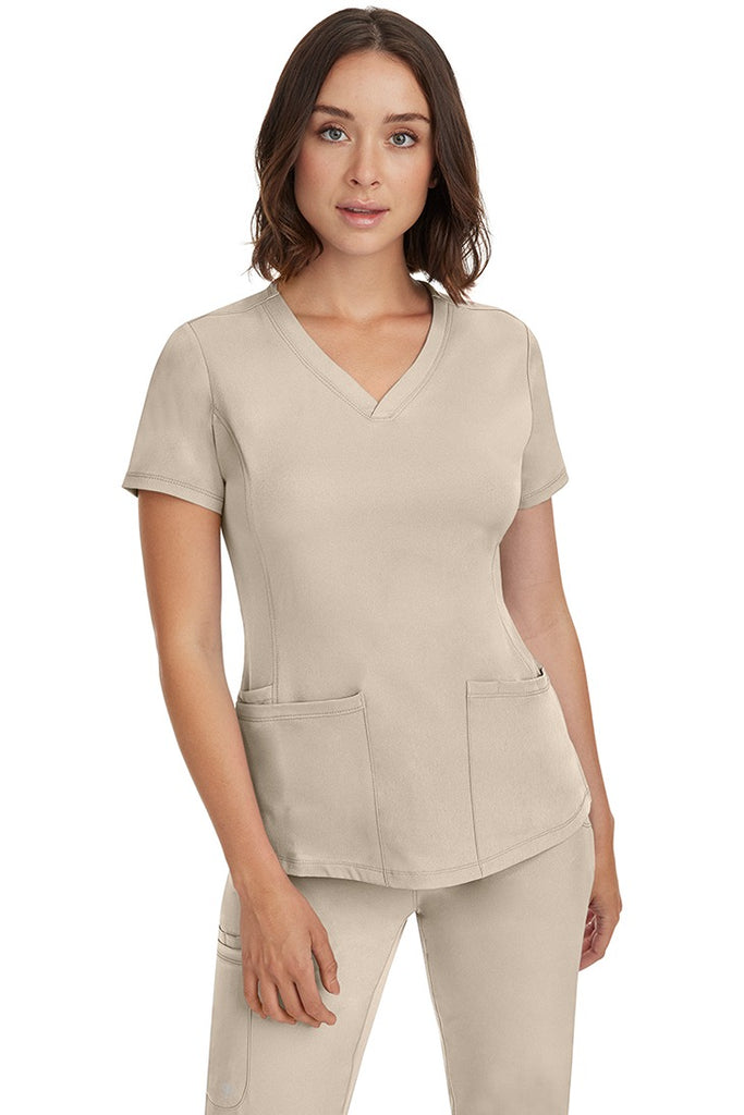 A young female Medical Transcriptionist wearing an HH-Works Women's Monica Multi-Pocket Scrub Top in Khaki size XL featuring a slightly curved, stylish v-neckline.