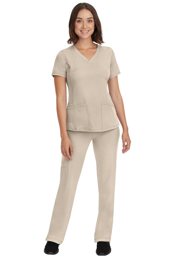 A young female Medical Coding Specialist wearing an HH-Works Women's Monica Multi-Pocket Scrub Top in Khaki size 2XL featuring an easy care fabric that is quick drying, moisture wicking, & super flexible.