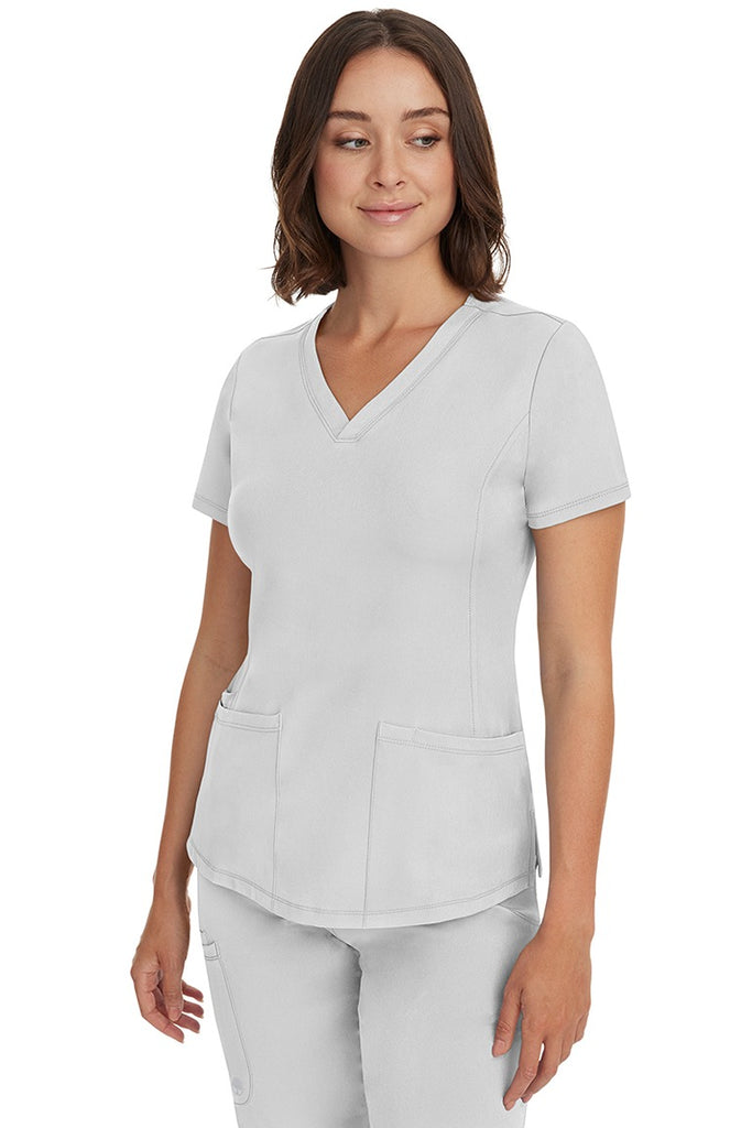 A young female healthcare professional wearing a HH-Works Women's Monica Multi-Pocket Scrub Top in White featuring a center back length of 24".
