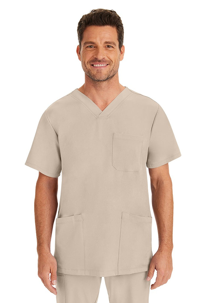 A young male nurse wearing an HH-Works Men's Matthew V-Neck Scrub Top in Khaki featuring a v-neckline & short sleeves.