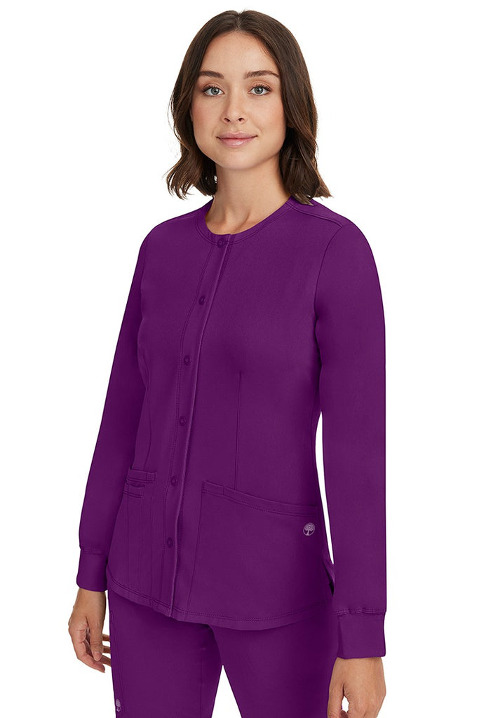A young female CNA wearing an HH-Works Women's Megan Snap Front Scrub Jacket in Eggplant featuring side slits for additional range of motion.