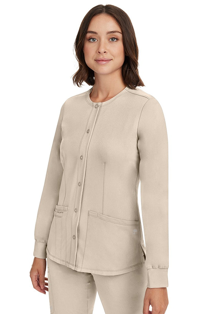 A young female CNA wearing an HH-Works Women's Megan Snap Front Scrub Jacket in Khaki featuring side slits for additional range of motion.
