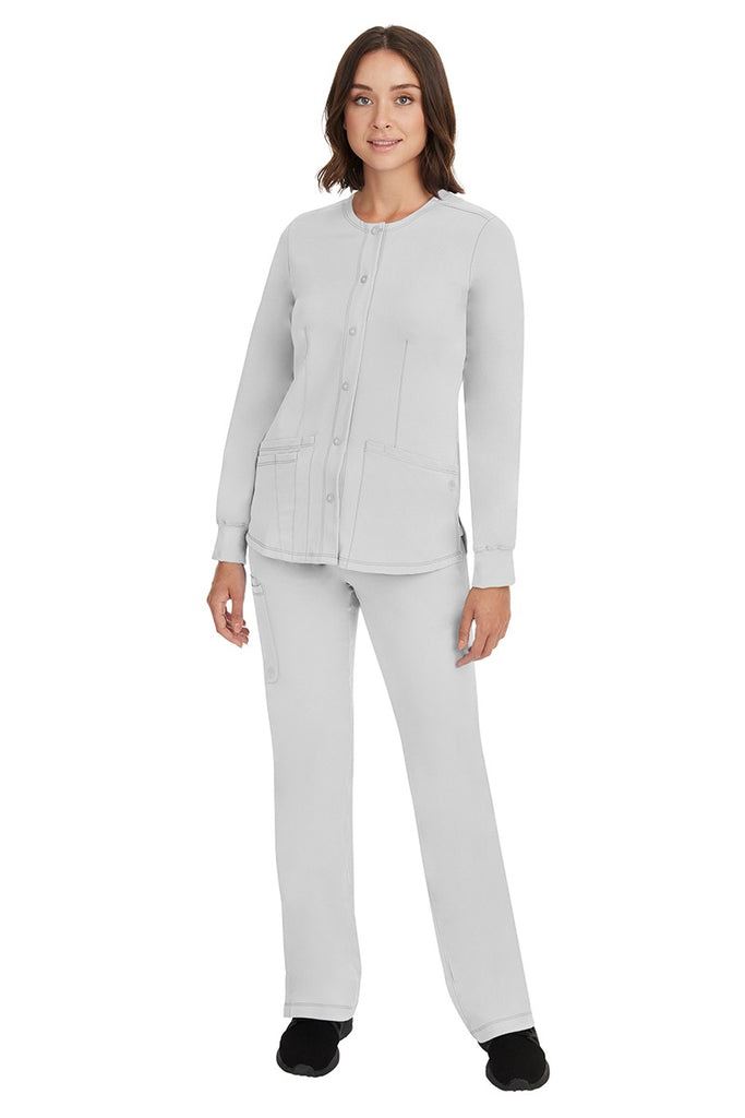 A young female Home Care Registered Nurse wearing an HH-Works Women's Megan Snap Front Scrub Jacket in White featuring yoga knit cuffs to ensure a flattering and comfortable fit.