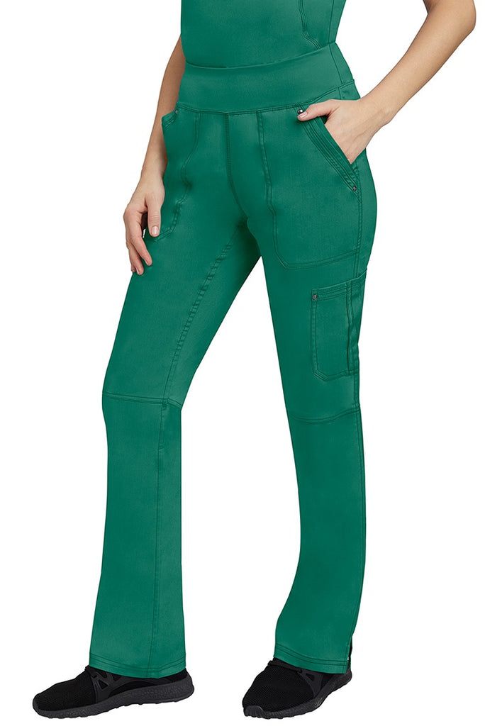 A young Home Care Registered Nurse wearing a pair of Purple Label Women's Tori Yoga Waistband Scrub Pants in Hunter Green featuring 1 outer cargo pocket on the wearer's left side pant leg.