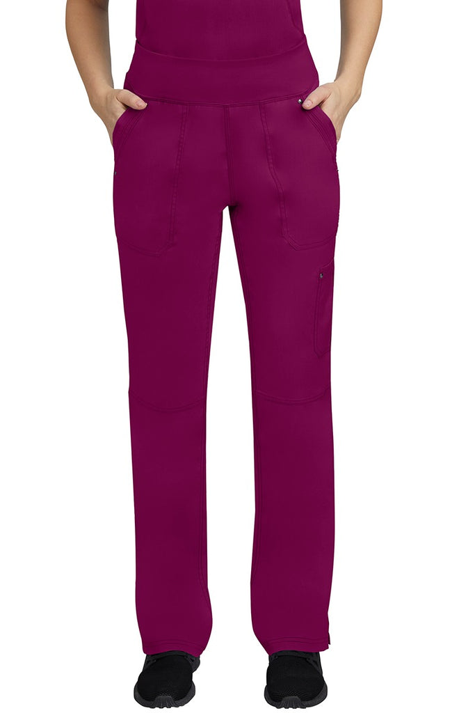 A young female LPN wearing a Purple Label Women's Tori Yoga Waistband Scrub Pant in Wine featuring 2 front side-entry pockets with grommet details.