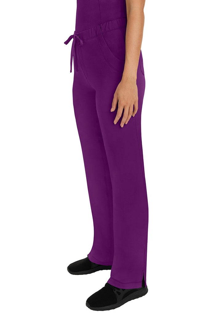 A woman Home Care Registered Nurse wearing a pair of HH-Works Women's Rebecca Multi-Pocket Drawstring Pants in Eggplant featuring side slits for additional range of motion.