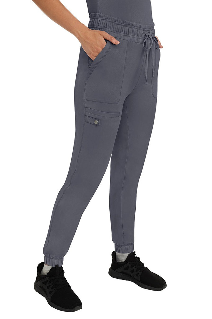 A female LPN wearing an HH Works Women's Renee Jogger Scrub Pant in Pewter  featuring 2 front patch pockets & 1 cargo pocket the wearer's right side leg.