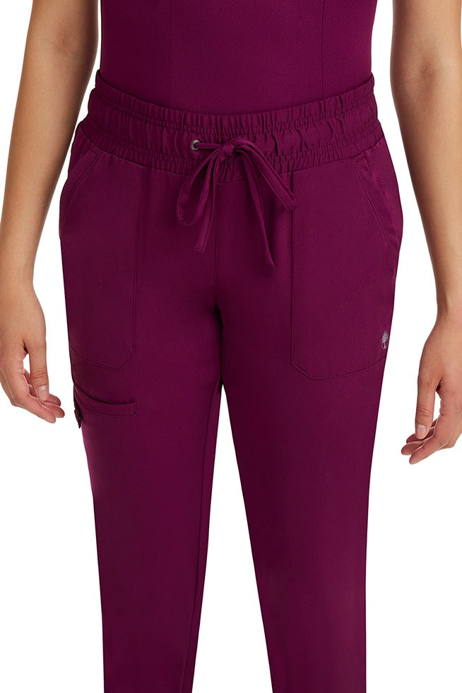 A female nurse wearing a pair of the HH Works Women's Renee Jogger Scrub Pants in Wine featuring a total of 6 pockets for all of your on the go storage needs.