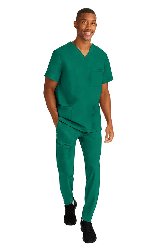 A young male RN wearing an HH-Works Men's Ryan Multi-Pocket Cargo Scrub Pant in Hunter Green featuring an easy care fabric that is quick drying, moisture wicking, and ultra-flexible.