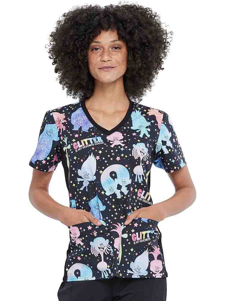 A young female Pediatric Nurse wearing a Tooniforms Women's V-neck Printed Scrub Top in "Glitter Trolls" featuring DreamWorks Animation's Trolls on a black background.