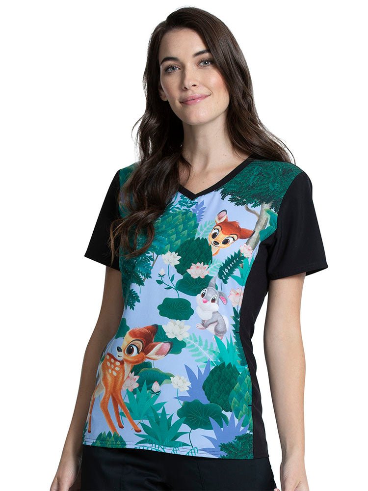A young female Pediatric Nurse wearing a Tooniforms Women's V-neck Printed Scrub Top in "Forest Frolic" featuring a banded solid v-neckline & short sleeves.