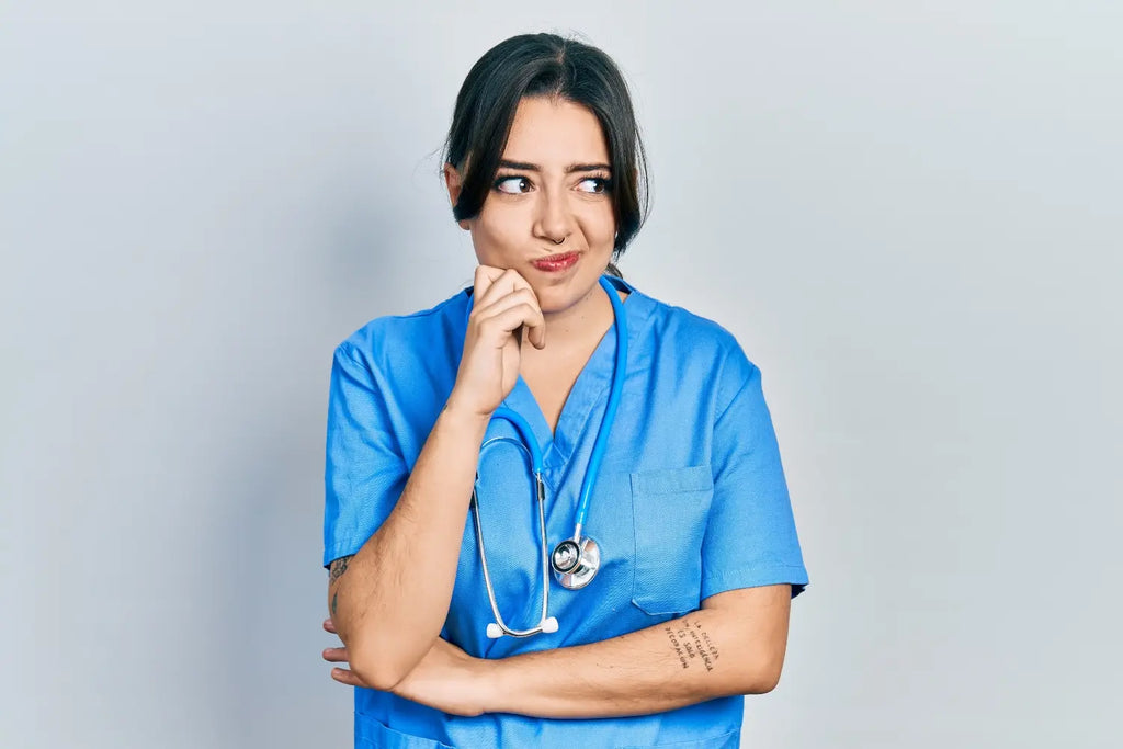 A young female Nurse Practitioner wearing Ceil Blue scrubs on a light grey background.