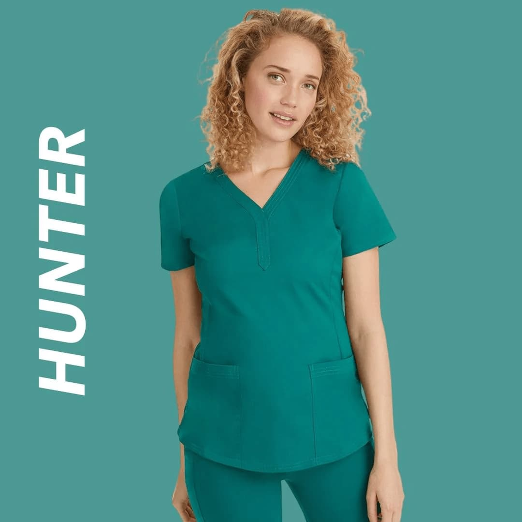 A young female Anesthesiologist wearing Hunter Green scrubs on a light green background. 