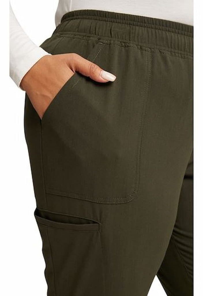 A young female Medical Assistant wearing a pair of Vince Camuto Women's Mid Rise Scrub Joggers in Heathered Olive size 3XL featuring an elastic-reinforced drawstring to ensure a comfortable all day fit.