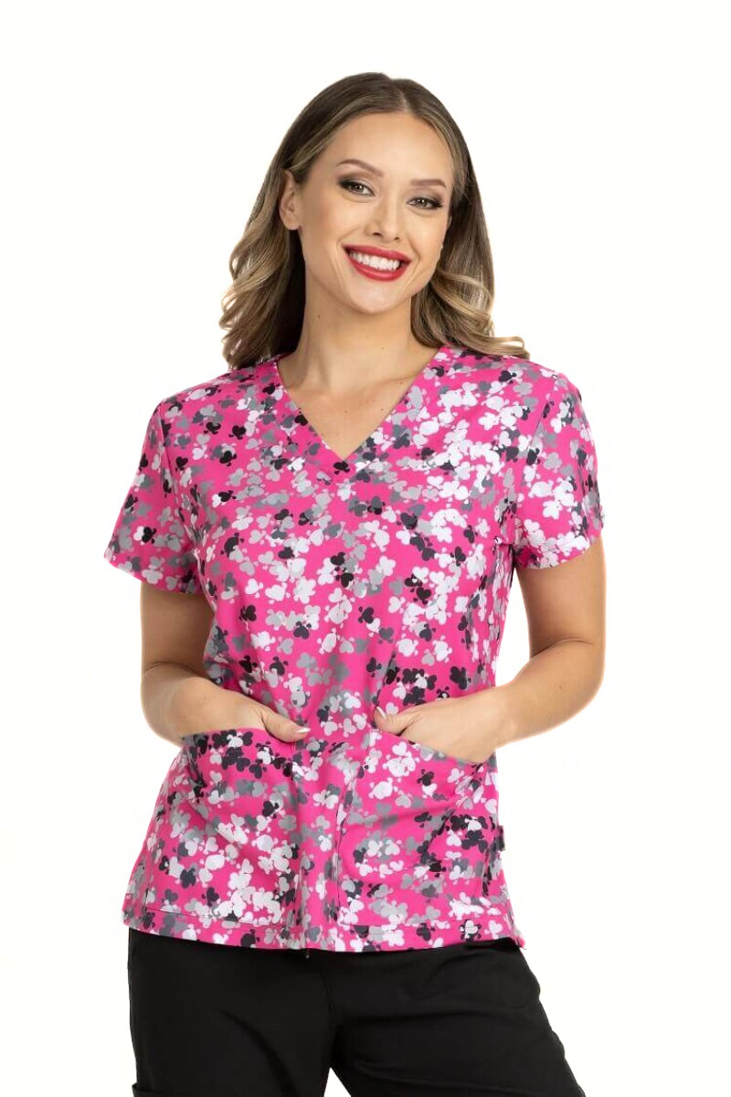 A young female Medical Assistant wearing a Meraki Sport Women's Print Scrub Top in "Love Crushin" size Medium featuring a v-neckline & short sleeves.