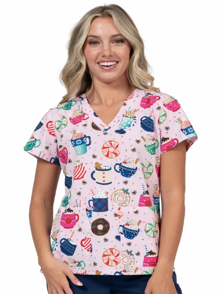 A young female Pediatric Nurse wearing a Meraki Sport Women's Print Scrub Top in "Mug-Nificent" featuring side slits for increased range of motion.