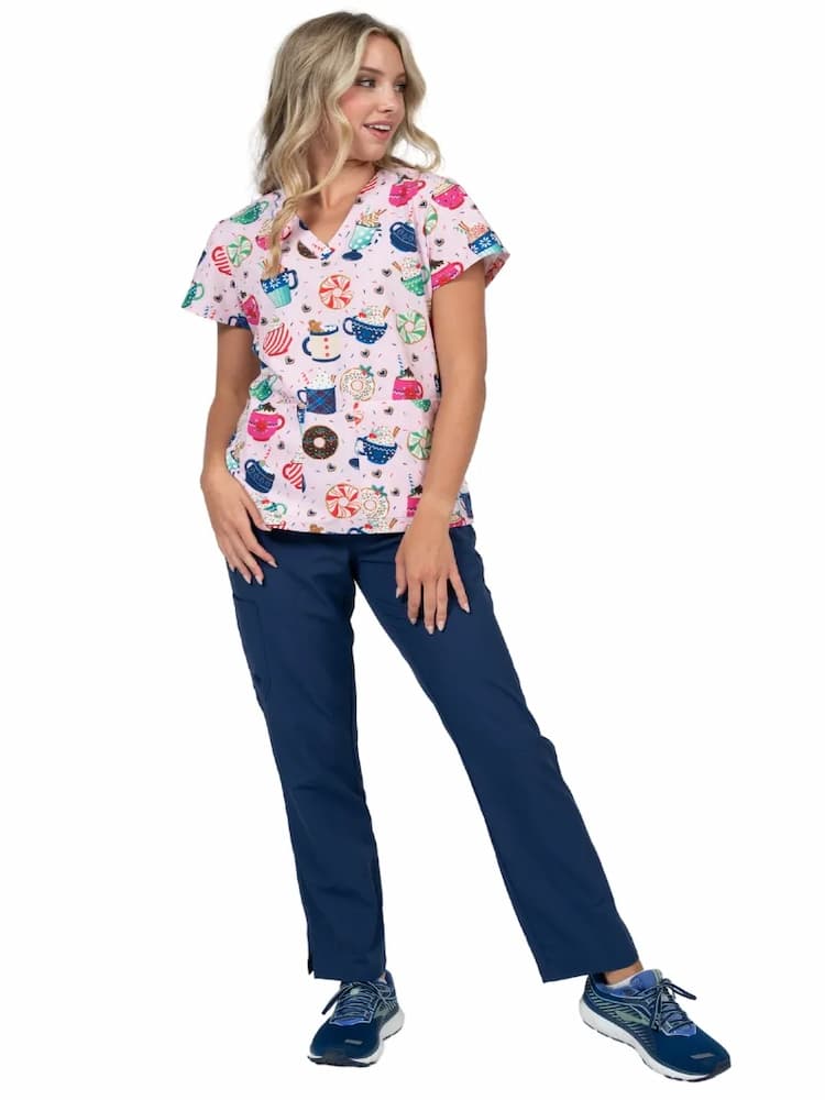 A full body image of a young female Pediatrician wearing a Meraki Sport Women's Print Scrub Top in "Mug-nificent" featuring a contemporary fit.