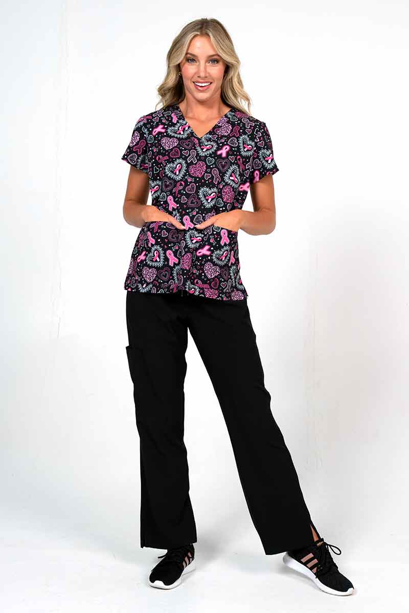 A young female Psychiatric Nurse  wearing a Meraki Sport Women's Breast Cancer Awareness Print Scrub Top in "Pink Strength"  featuring a nuique polyester/spandex blended stretch fabric.
