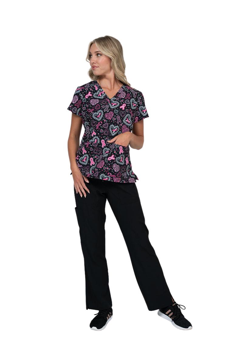 An image of a young female Oncology Nurse wearing a Meraki Sport Women's Breast Cancer Awareness Printed Scrub Top in "Pink Strength" featuring 2 front patch pockets and side slits.