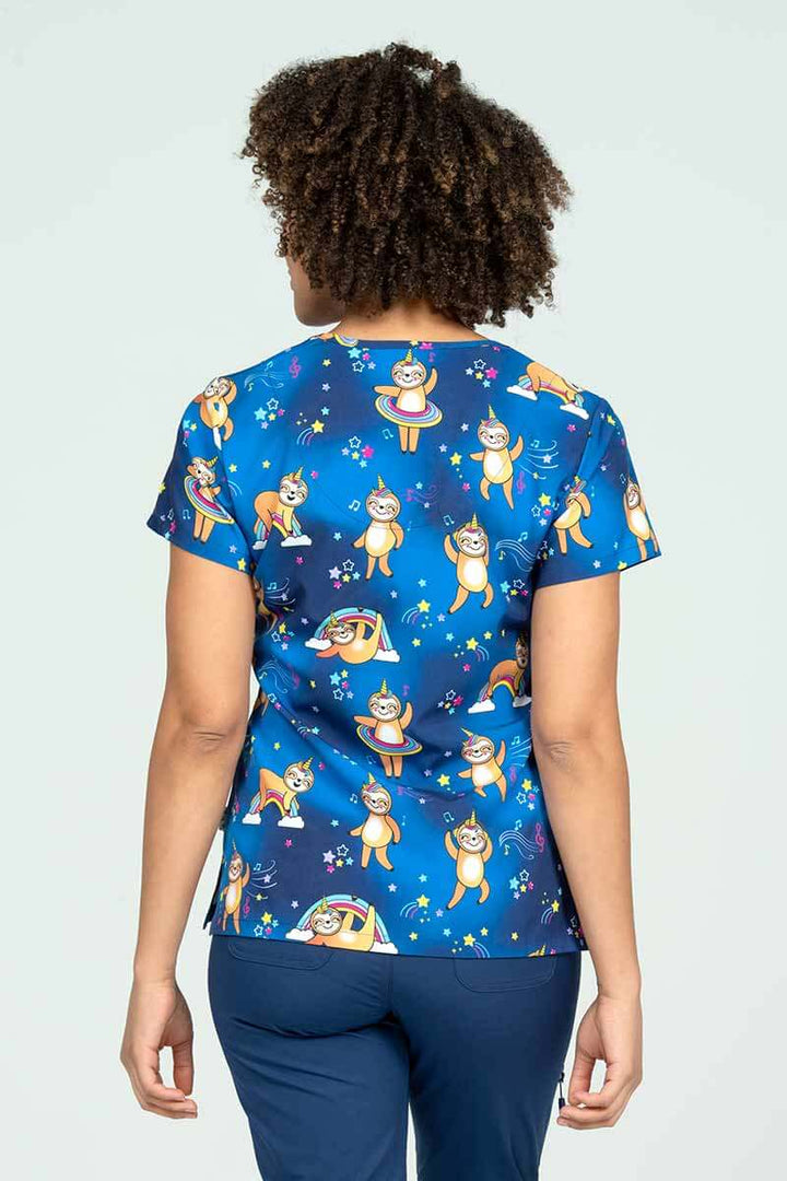 A young female pharmacist wearing a Meraki Sport Women's Print Scrub Top in "Sloth Squad" featuring a unique 4-way stretch fabric designed to move with your body all day long.