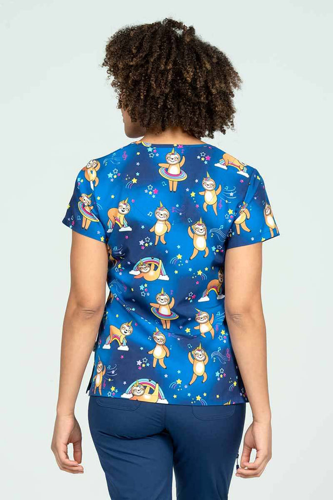 A young female pharmacist wearing a Meraki Sport Women's Print Scrub Top in "Sloth Squad" featuring a unique 4-way stretch fabric designed to move with your body all day long.