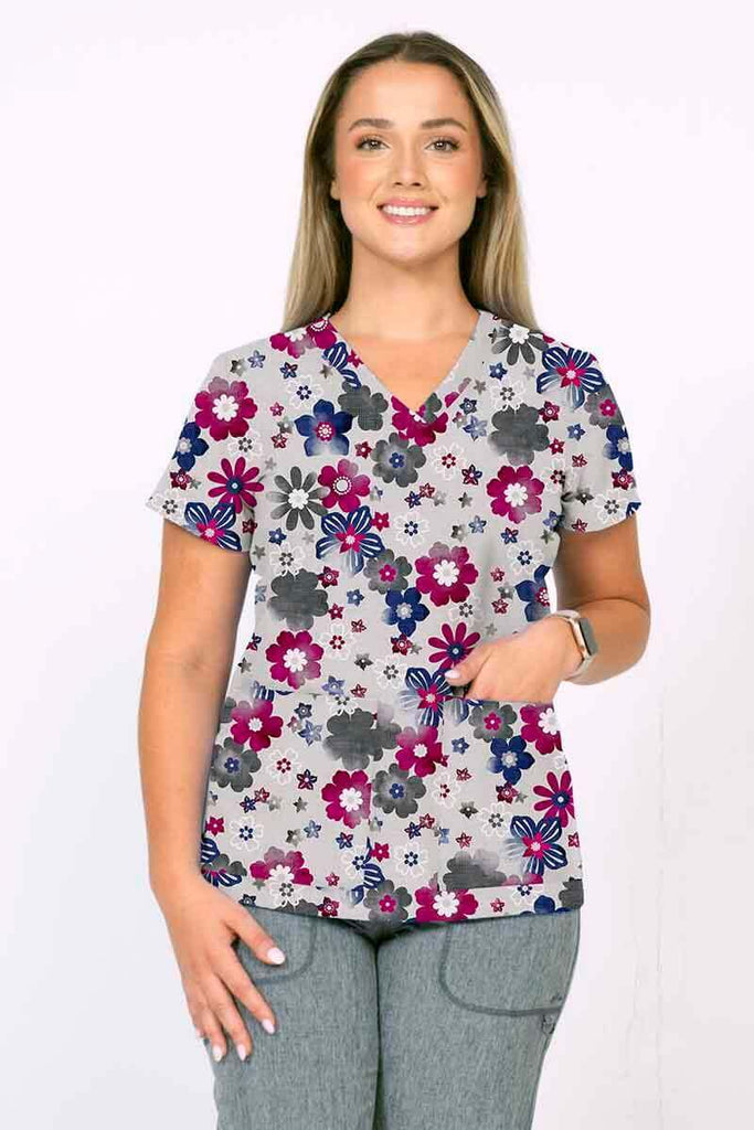 A young female Nurse Practitioner wearing a Meraki Sport Women's Print Scrub Top in "Splash of Heather" size small featuring a v-neckline & short sleeves.