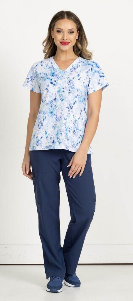 A full body image of a female RN wearing a Women's Print Scrub Top from Meraki Sport in "Tie Dye Obsession" size Small featuring 2 front patch pockets & shoulder yokes for a flattering shape.