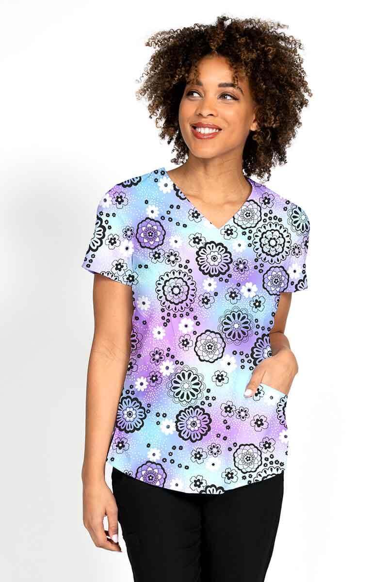 A young female Nurse Practitioner wearing a Meraki Sport Women's Print Scrub Top in "Lovely Lavender" featuring front & back princess seams.