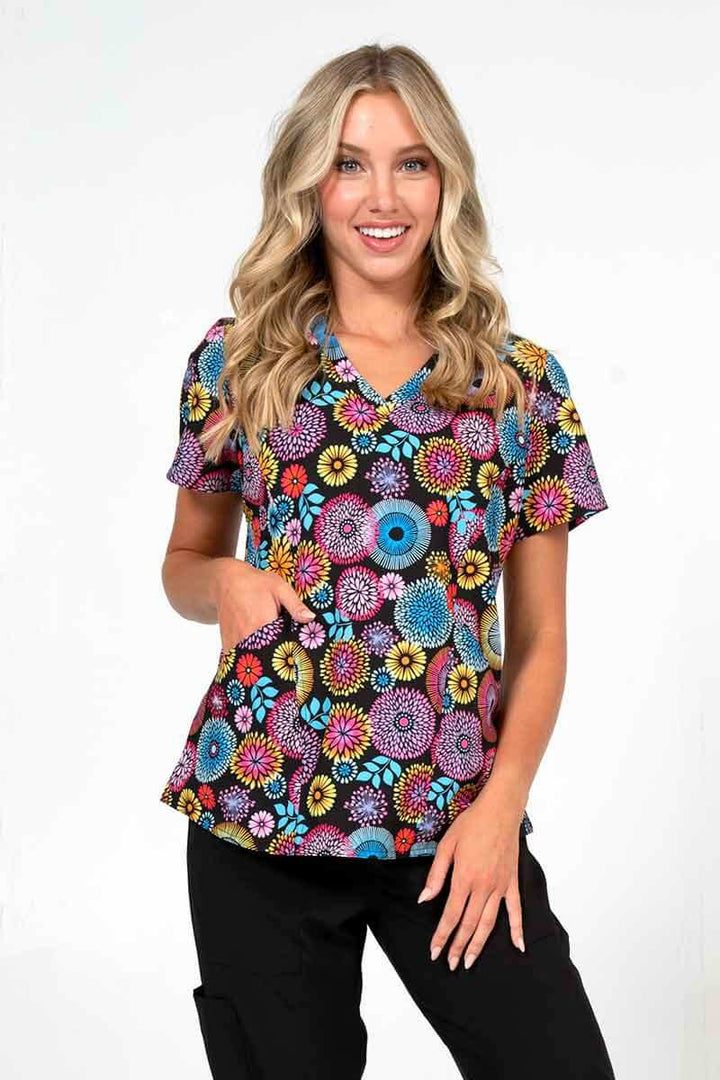 A young female nurse wearing a Meraki Sport Women's Print Scrub Top in "Petal Affair" size small featuring a v-neckline & short sleeves.