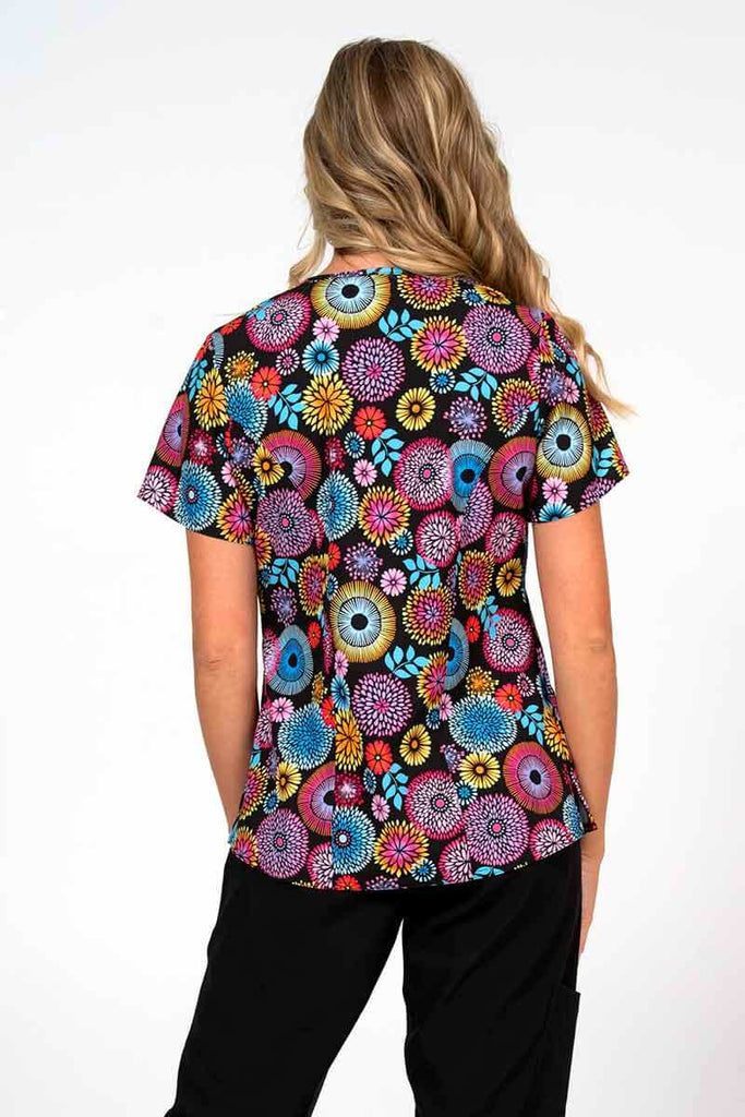 A young female Nurse Practitioner wearing a Women's Print Scrub Top from Meraki Sport in "Petal Affair" size medium featuring shoulder yokes & side slits for additional range of motion.