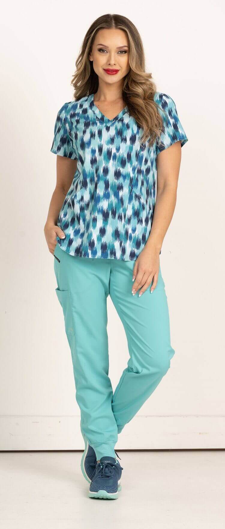 A full body image of a young female LPN wearing a Meraki Sport Women's Print Scrub Top in size Small featuring shoulder yokes for shaping & side slits for additional range of motion.