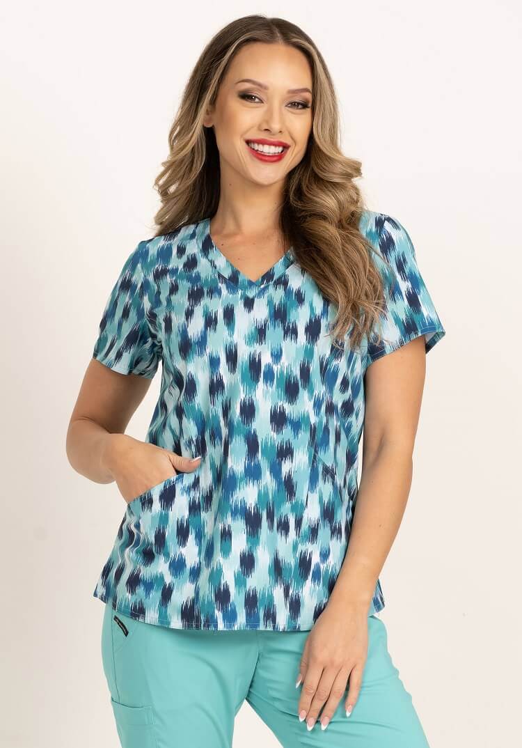 A young female Pediatrician wearing a Meraki Sport Women's Print Scrub Top in "Seafoam Oasis" size Medium featuring 2 front patch patch pockets & a V-neckline.