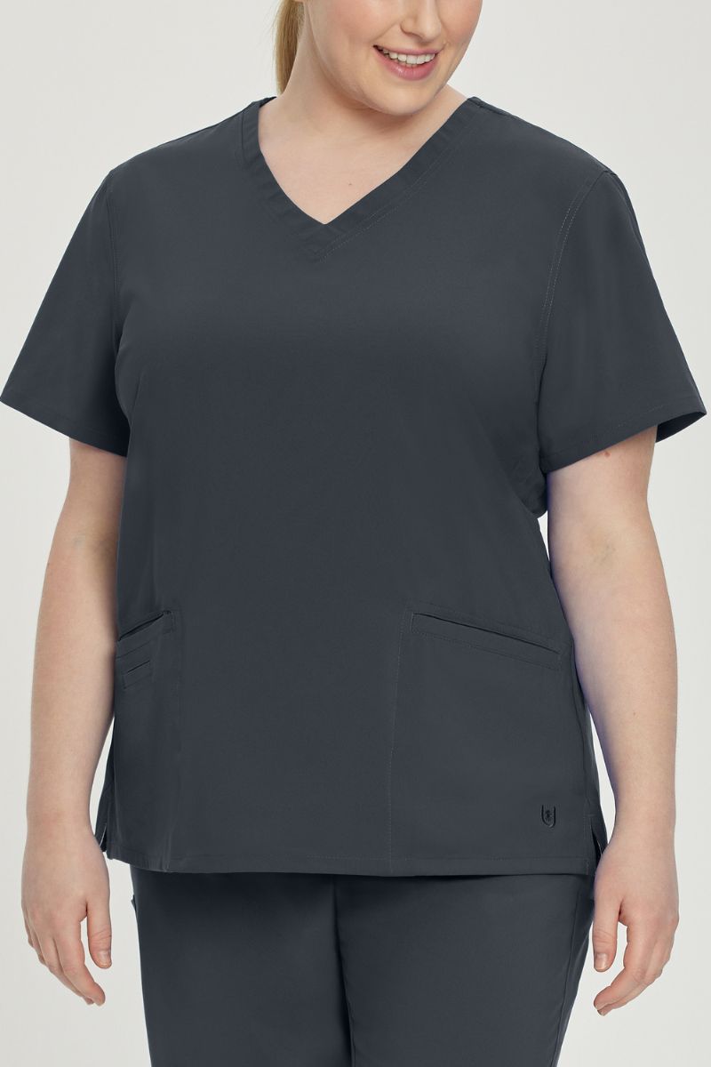 A young female Lab Tech wearing an Urbane Performance Women's Motivate V-neck Scrub Top in Graphite size 5XL featuring tonal stitching and bust darts.