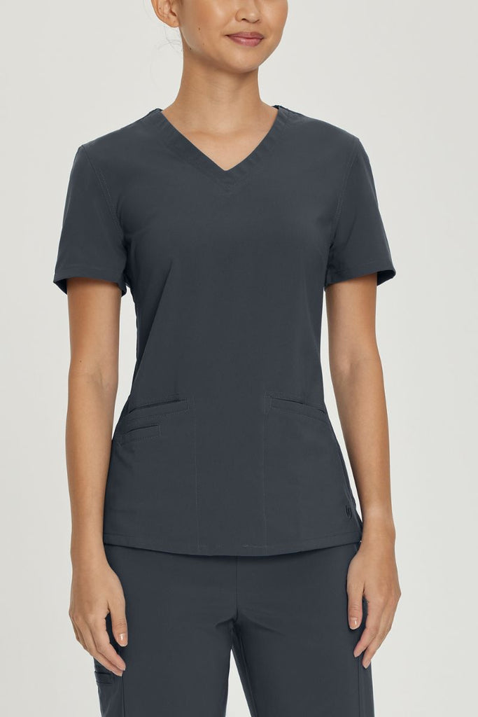 A young female LPN wearing an Urbane Performance Women's Motivate V-neck Scrub Top in Graphite size Small featuring a two front angled welt pockets.