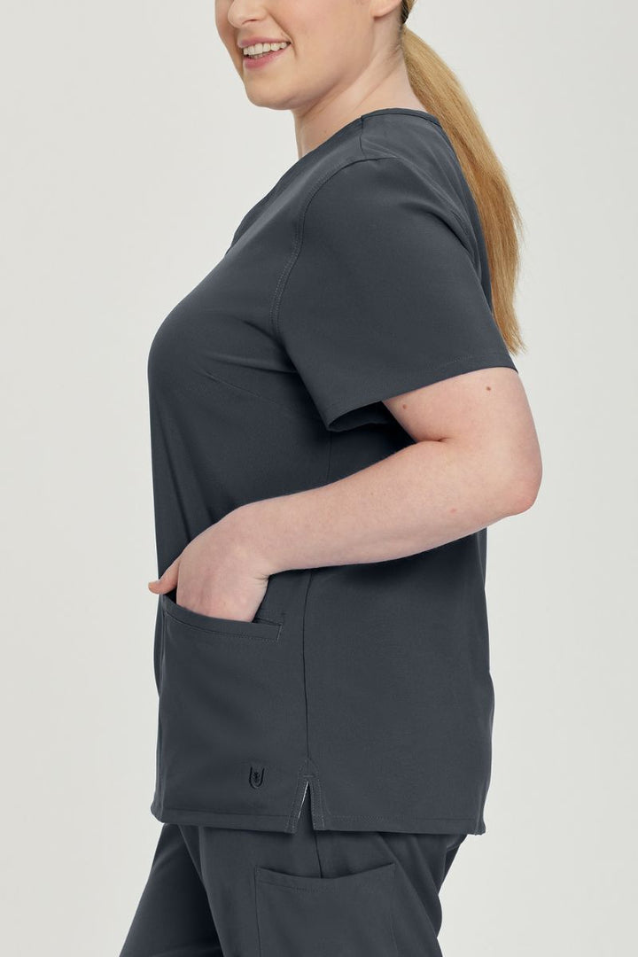 A young female Pharmacy Tech wearing an Urbane Performance Women's Motivate V-neck Scrub Top in Graphite featuring a total of 3 pockets.