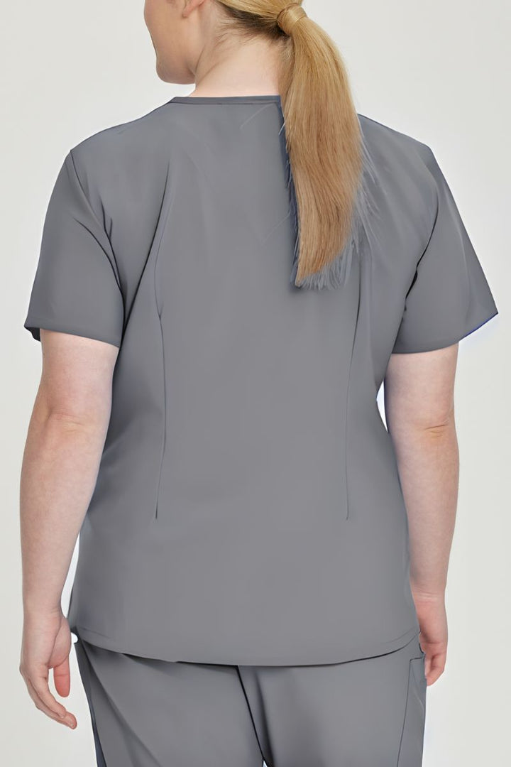 A young female Medical Assistant wearing an Urbane Performance Women's Motivate V-neck Scrub Top in Steel size 3XL featuring a unique, 4-way stretch fabric.