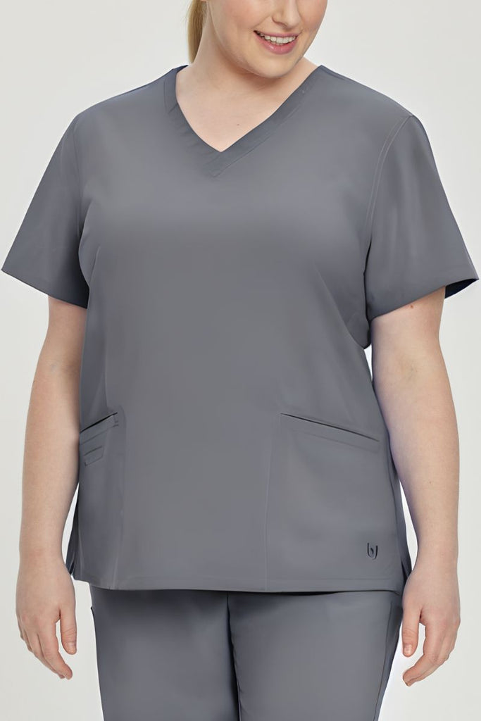 A young female Lab Tech wearing an Urbane Performance Women's Motivate V-neck Scrub Top in Steel Grey size 5XL featuring tonal stitching and bust darts.