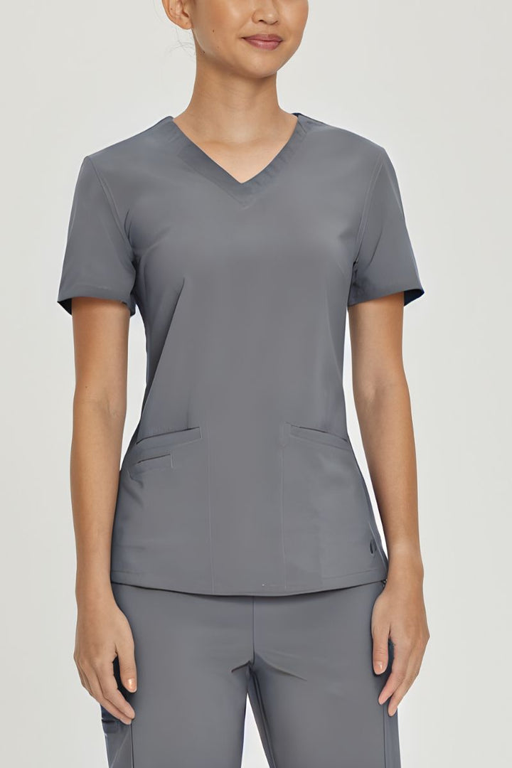 A young female LPN wearing an Urbane Performance Women's Motivate V-neck Scrub Top in Steel size Small featuring a two front angled welt pockets.