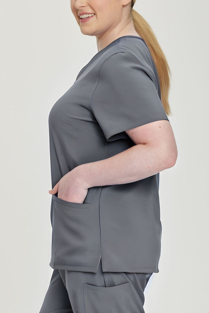 A young female Pharmacy Tech wearing an Urbane Performance Women's  Motivate V-neck Scrub Top in Steel Grey featuring a total of 3 pockets.