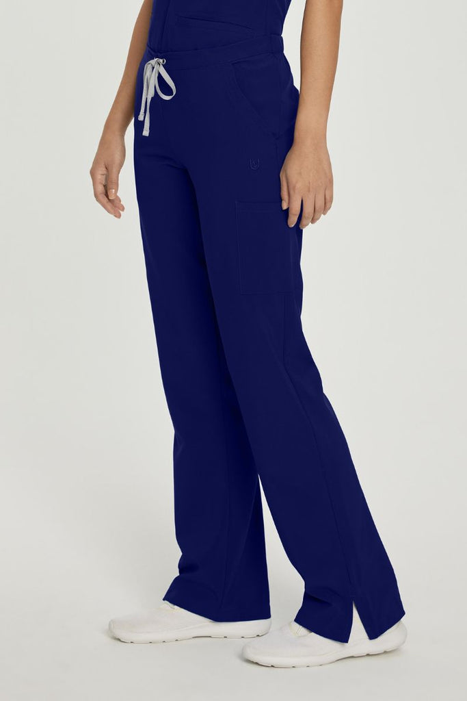 A young female Nurse wearing a pair of Urbane Performance Endurance Cargo Scrub Pants in True Navy featuring 6 pockets in total, for all of your on the job storage needs.
